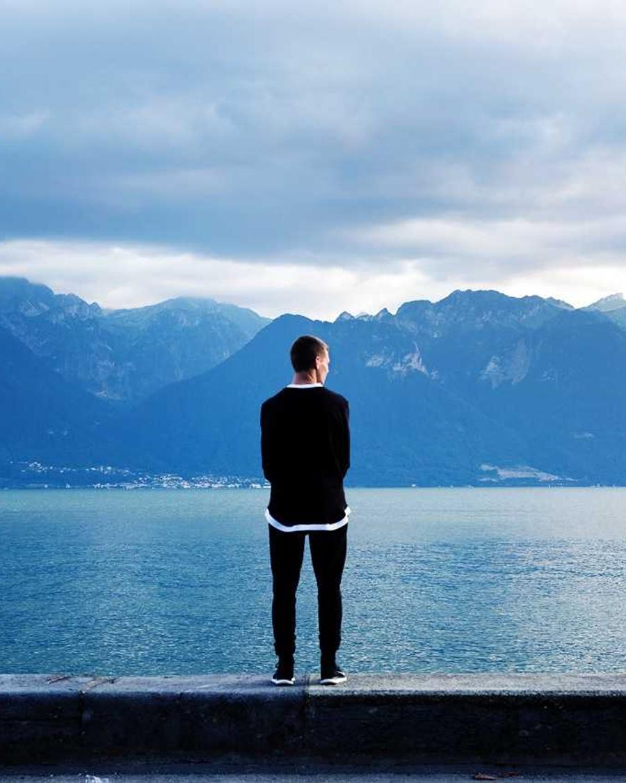 Petteri Mäntynen de dos, face à un lac de montagne sous un ciel couvert